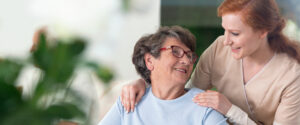 Close-up of a tender caregiver with her hands on the shoulders of a senior woman inside her home. 
