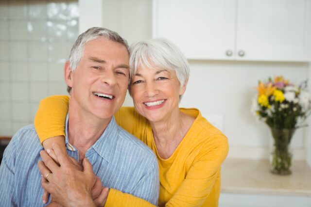 Smiling elderly couple hugging in their clean white kitchen