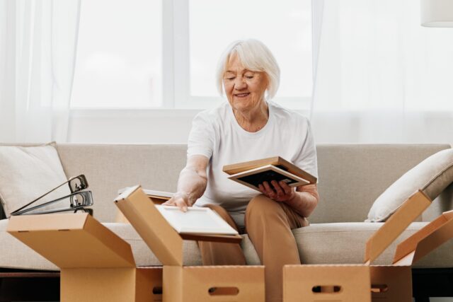 Elderly woman sitting on a sofa at home with boxes.